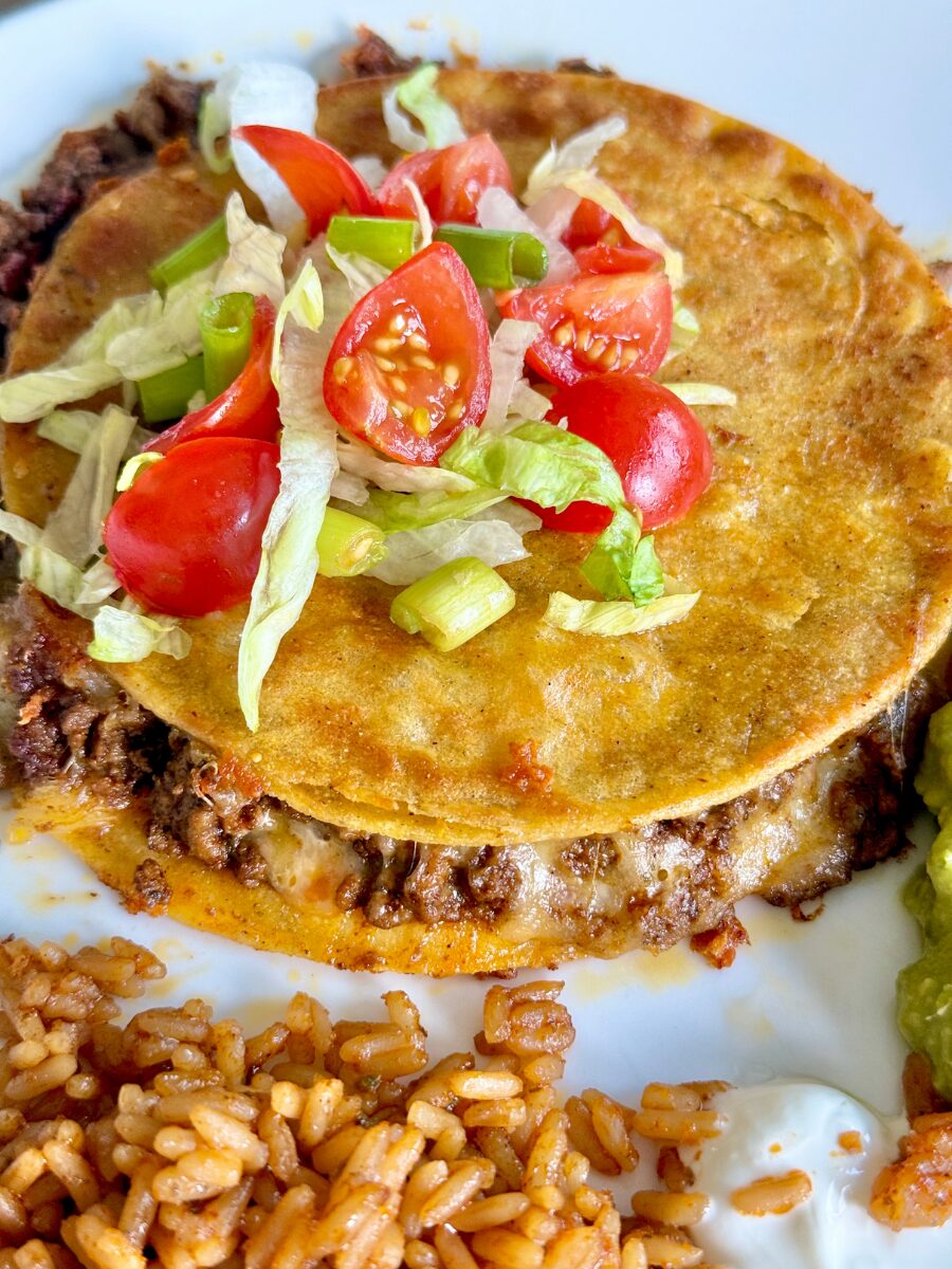 Cheesy beef quesadilla with chopped tomatoes and green onions and shredded lettuce, sitting on top of white plate with Mexican rice