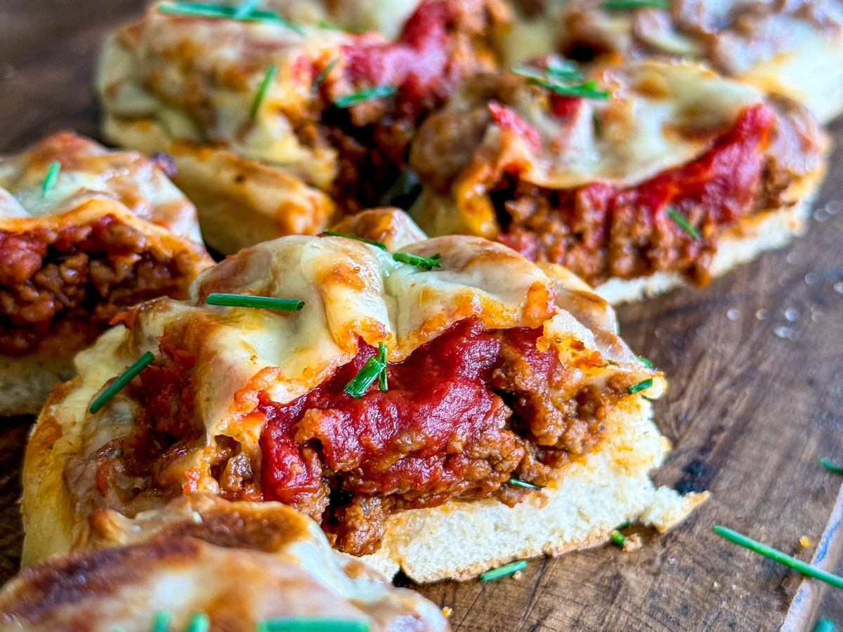 closeup of cooked pizza burgers cut in half to show inside mixture sitting on a wooden tray