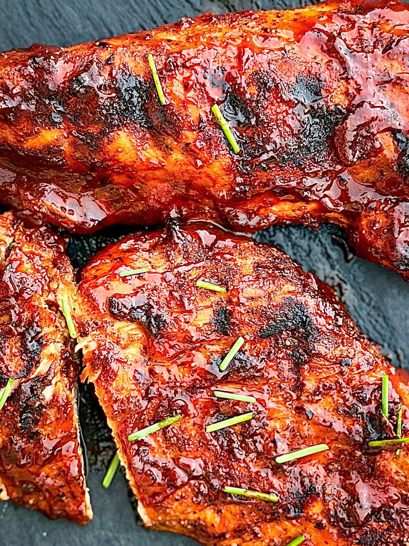 Grilled BBQ Chicken sitting on gray slate surface with cut chives