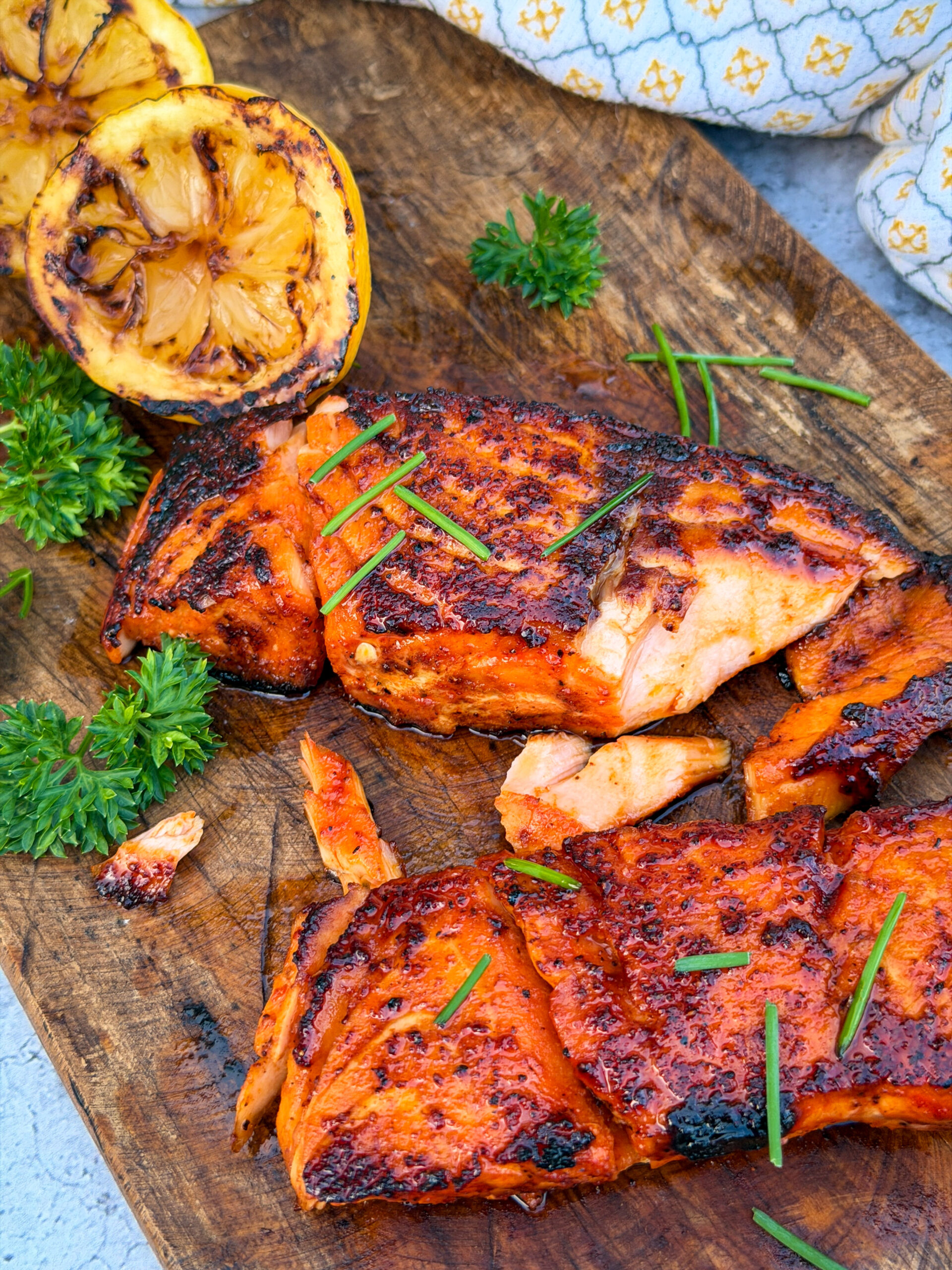 Grilled lemon halves sitting next to Maple Bourbon Salmon on wood surface wiht parsley